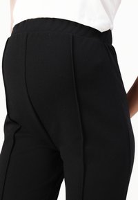 Pantaloni neri realizzati in tessuto testurizzato, con vita alta, frontale plissettato e tasche laterali per un tocco in più.