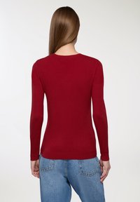 Czerwona długi rękaw sweter z okrągłym dekoltem, dopasowany krój i ściągacz u dołu. Gładka faktura, minimalne detale i brak widocznych wzorów.