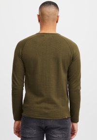 Olijfgroen shirt met lange mouwen van gestructureerde stof, voorzien van raglanmouwen en een klein merketiket in de linkernaad.