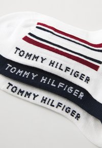 Bomullssockor med "TOMMY HILFIGER"-logotyp i svart på vit och marinblå bakgrund, med röda och marinblå ränder vid överkanten.