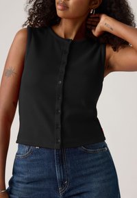 Black ribbed sleeveless top featuring a round neckline and front button closure. Complemented by fitted styling and a cropped length.