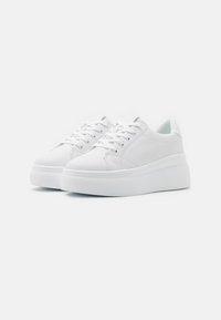 Baskets blanches avec une semelle en caoutchouc texturé et un col rembourré, présentant une tige en cuir lisse et des lacets plats pour la fermeture.