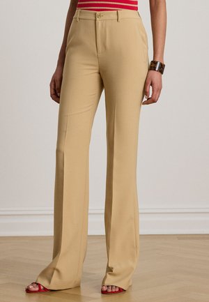 Beige Hosen mit weitem Bein und vorderen Taschen, knopfbarer Bund, getragen mit roten Riemchensandalen und einem Armband aus Schildpatt am rechten Handgelenk.