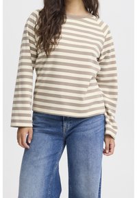 Pull long à rayures beige et crème, à col rond. Coupe loose, détails de poignets côtelés, associé à un jean large bleu clair.