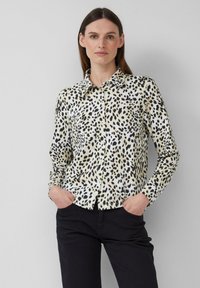 Chemise à motif léopard en crème et noir, dotée d'un col classique, de manches longues et d'une coupe décontractée. Portée avec un pantalon sombre.