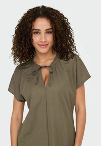 Olivgrünes, locker sitzendes Kleid mit rundem Ausschnitt und Bindeband. Kurze Ärmel, weicher Stoff und eine Knopfleiste mit dezentem V-Ausschnitt.