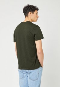 Donkergroene katoenen t-shirt met korte mouwen, ronde hals en een relaxte pasvorm. Draag het met lichtblauwe jeans, gezien vanuit de achterkant.