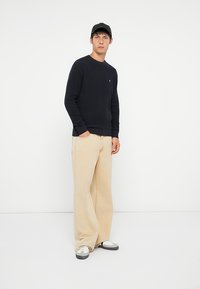 Marineblå strikkegenser, avslappet passform, rund hals; kombinert med beige vide bukser. Svart caps, grå og hvite joggesko fullfører antrekket.