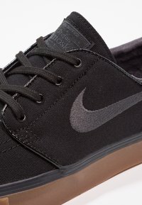 Baskets de skate noires en toile avec une tige texturée et un logo Nike gris emblématique. Comprend des œillets noirs et une semelle en caoutchouc gomme.