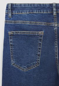Jean en denim bleu foncé avec une poche arrière à couture orange, présentant une texture lisse et un design classique à cinq poches.