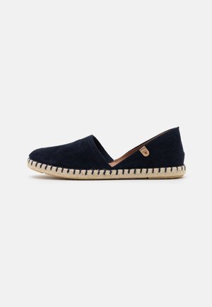 Espadrille en daim bleu marine avec semelle tissée beige et couture latérale, avec une petite étiquette en cuir marron clair sur le côté.
