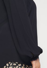 Marineblauwe blouse met lange mouwen, een losse pasvorm en gathered manchetten. Gladde textuur, licht gebogen zoom, gecombineerd met een rok met bloemenpatroon.