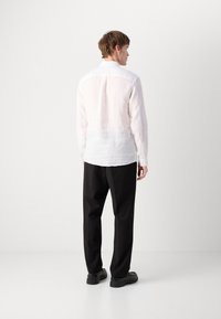 Camisa leve de linho rosa com mangas longas, fecho de botão e bainha arredondada, combinada com calças pretas e sapatos pretos.