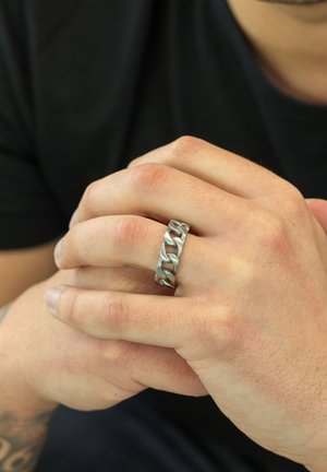 Silver chain-link ring featuring textured patterns, placed on a hand with fingers interlaced, skin tones visible.
