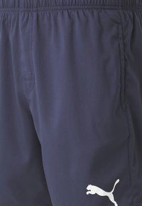 Shorts de sport bleu marine en tissu léger, dotés d'une taille élastique et d'un logo Puma blanc bien visible sur le bas.