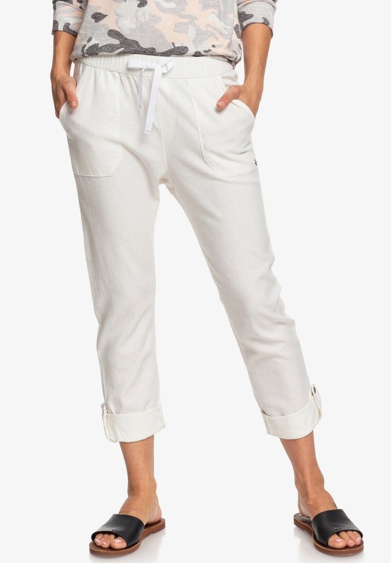 Valkoiset pellavahousut, joissa on joustava vyötärö, nauhakuja, kaksi etutaskua ja kiero lahje. Yhdistetty mustiin liukusandaaleihin.