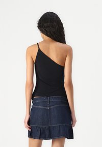 Black one-shoulder top made of stretch fabric, paired with a denim skirt featuring a frilled hem and subtle stitching details.