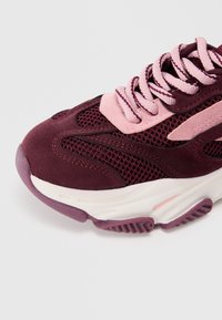 Baskets bordeaux avec tige en mesh et en daim, lacets roses, semelle intermédiaire crème et semelle extérieure violette texturée. Offre un design sportif.