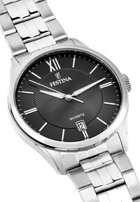 Sudraba nerūsošā tērauda pulkstenis ar melnu teksturētu ciparnīcu, baltām stundu marķieriem un datuma displeju pulksten 6. Kvarts kustība.