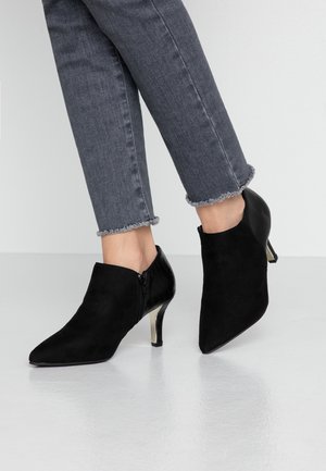 Kvinde iført grå jeans med frynset kant og sorte ruskindsstøvler med spids tå, kitten hæle og sidelommer med lynlås.