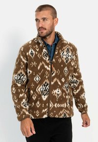Braune Fleecejacke mit elfenbeinfarbenen und schwarzen geometrischen Mustern, hohem Kragen und Frontreißverschluss; verfügt über Seitentaschen und elastische Bündchen.