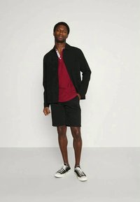 Black jacket, red polo shirt with white collar, black shorts, and black sneakers. Simple design, casual materials, and fitted silhouette.
