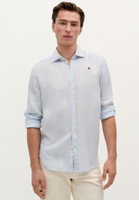 Lysblå button-up skjorte lavet af blødt stof, med klassisk krave og oprevne ærmer. Lille broderet logo på brystet.