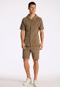 Bruine gestructureerde short-sleeve shirt met grote kraag en knopen, gecombineerd met bijpassende shorts. Draagt witte sneakers.