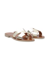 Metallisch goldene Riemensandalen mit flacher Sohle, die zwei breite Riemen und eine glatte Lederinnensohle aufweisen, vor einem weißen Hintergrund.
