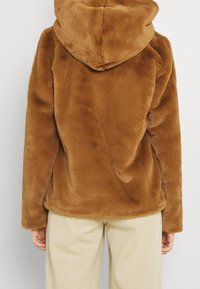 Hoodie en polaire marron avec une texture douce et une grande capuche, présentant une coupe décontractée et de longues manches. Design minimaliste, sans fermetures visibles.