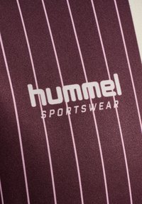 Bordowy materiał sportowy z cienkimi różowymi pionowymi paskami. Zawiera logo "hummel" oraz napis "SPORTSWEAR" w białej czcionce. Gładka faktura.