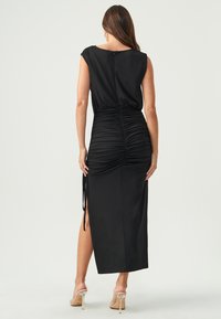 Schwarzes Kleid mit kurzen Ärmeln, gerafften Details am Rücken und seitlichen Schlitzen. Glattes Material mit taillierter Silhouette und knielanger Länge.