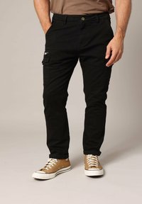 Zwarte cargo broek met een slim fit, voorzien van een zijzak met een rits en een knoopsluiting, gecombineerd met tan hoge sneakers.