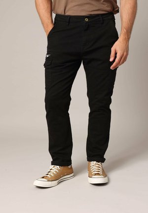 Zwarte cargo broek met een slim fit, voorzien van een zijzak met een rits en een knoopsluiting, gecombineerd met tan hoge sneakers.