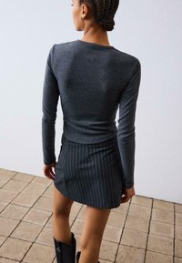 Siva majica z dolgimi rokavi s prilegajočim se krojem, v kombinaciji s kratko črno krilom s črtami. Gladka tekstura, sproščen stil in minimalno okrasje.