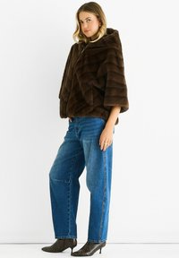 Woman wearing a dark brown faux fur cape, blue straight-leg jeans, and pointed-toe ankle boots with a snake print pattern.