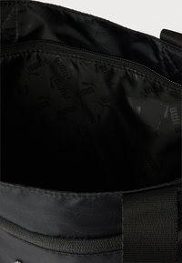 Black fabric bag interior with a zippered pocket and repeated Puma logo pattern on the lining.