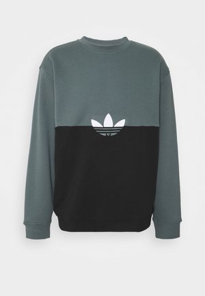 Bluza z okrągłym dekoltem i długimi rękawami, górna połówka w ciemnozielonym kolorze, dolna połówka czarna, z białym logo Adidas trefoil na środku klatki piersiowej.
