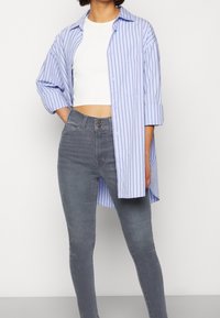 Camisa de manga larga a rayas azul y blanca con cuello, combinada con pantalones ajustados gris con cierre de botón en la parte delantera y bolsillos.