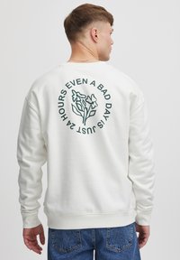 Hvid sweatshirt med grønne blomster grafikker og tekst på ryggen. Ribbetærmer og -kant; afslappet pasform med blød tekstur.