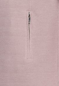 Prenda de color rosa claro con un patrón de espiga texturizado, cierre frontal con cremallera plateada. La tela tiene una profundidad sutil.