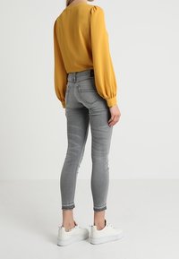 Žlutá blůza s nadýchanými rukávy, šedé skinny džíny a bílé tenisky. Hladká látka a přiléhavý střih zdůrazněný zezadu.