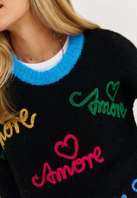 Czarny sweter z dzianiny z żywymi haftowanymi logo w kolorze różowym, zielonym, żółtym i niebieskim, z niebieskim ściągaczem i miękką teksturą.