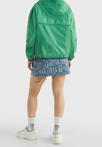 Zelená lehká bunda, džínová sukně s výrazným potiskem "TOMMY", bílé tenisky a vzorované ponožky. Důraz na neformální, sportovní designové prvky.