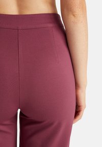 Bordové kalhoty s elastickým pasem a hladkým povrchem. Vyznačují se čistým designem, jemnými švy a přiléhavým střihem.