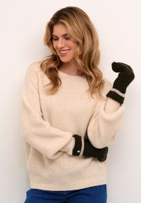 Beige strikket trøje med en løs pasform og ribbet tekstur, parret med mørkegrønne vanter med en kontrasterende stribe og knapdetalje.