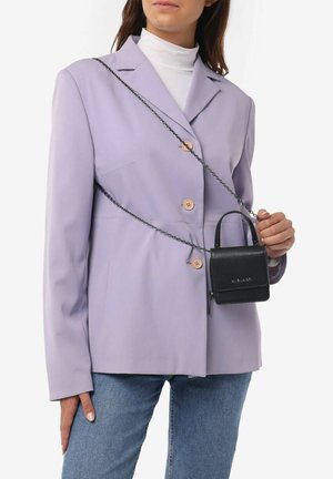 Sort crossbody taske med tekstureret overflade, rektangulær form og top-håndtag, båret over en lavendel blazer med runde knapper.