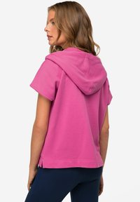 Felpa corta rosa con cappuccio, realizzata in tessuto morbido, caratterizzata da un orlo rilassato e fessure laterali per facilitare i movimenti.