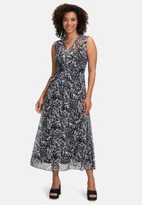Maxikleid mit schwarz-weißem Blumenmuster, V-Ausschnitt und ärmellosem Design. Glattes Material mit fließender Silhouette. Schwarze Plateausandalen.