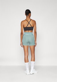 Reggiseno sportivo nero con spalline incrociate, abbinato a pantaloni corti atletici color verde menta. Include un marchio bianco sulla vita, evidenziando comfort e vestibilità.